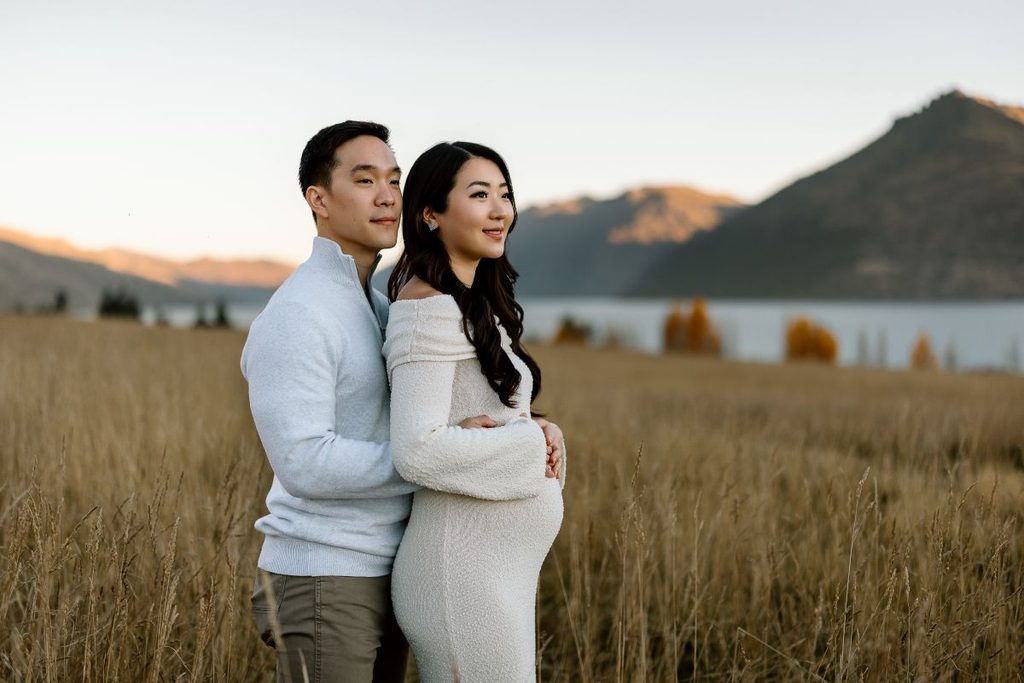 couple from Singapore during their babymoon to New Zealand, posing for a maternity photoshoot in Queenstown with the lake and mountains in the background