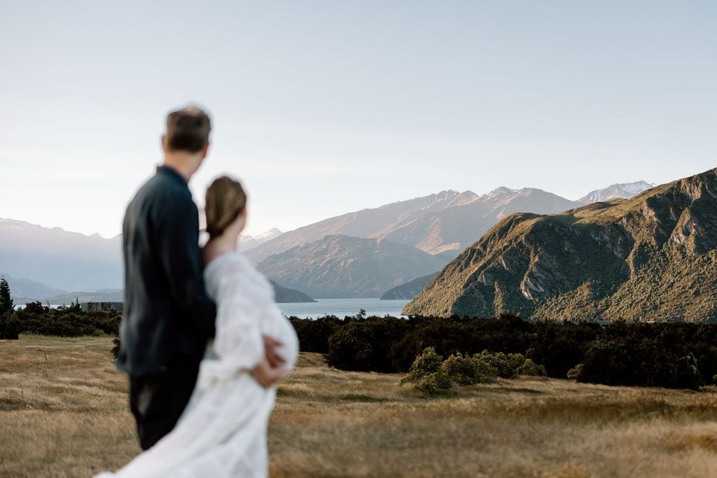 Expecting couple looking over the lake and mountains at Jason's Clearing in Lake Wanaka, New Zealand.
